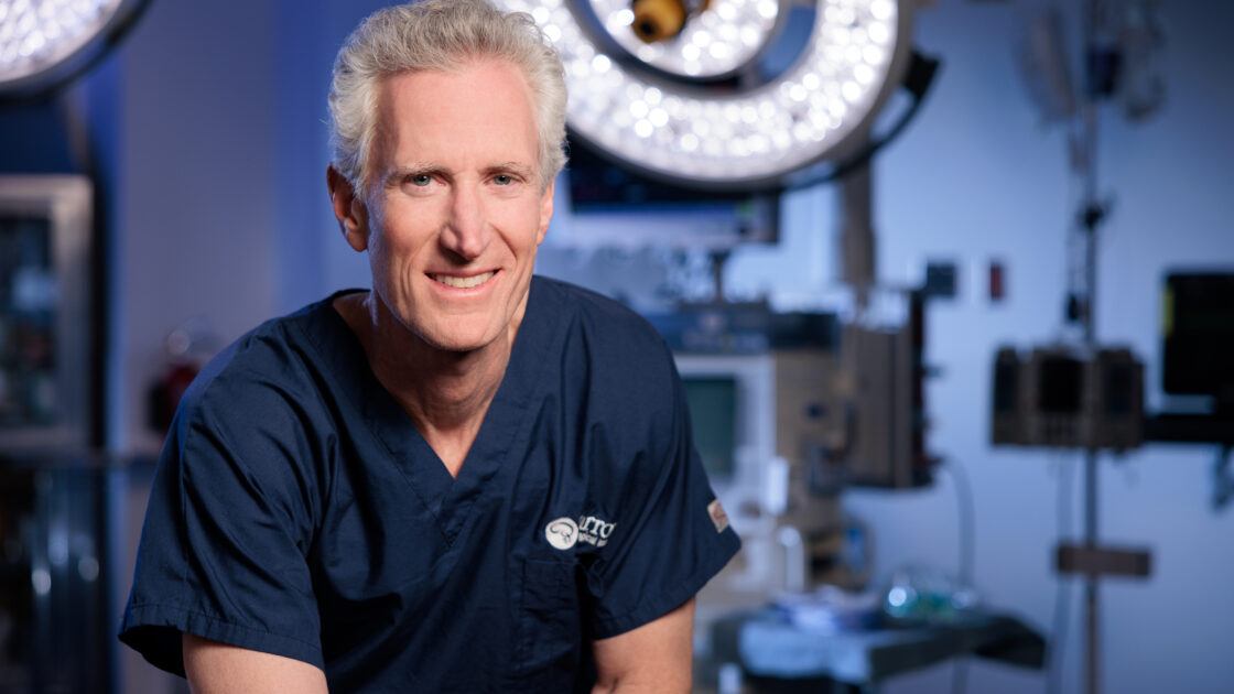 Portrait of Dr. Michael T. Lawton in the operating room. He is wearing scrubs and smiling at the camera.