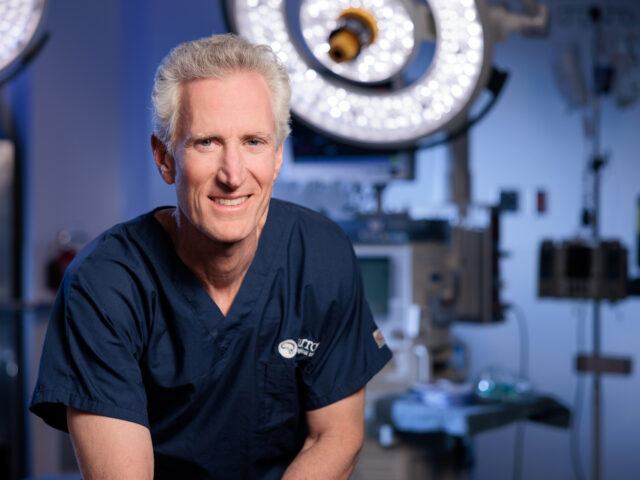 Portrait of Dr. Michael T. Lawton in the operating room. He is wearing scrubs and smiling at the camera.