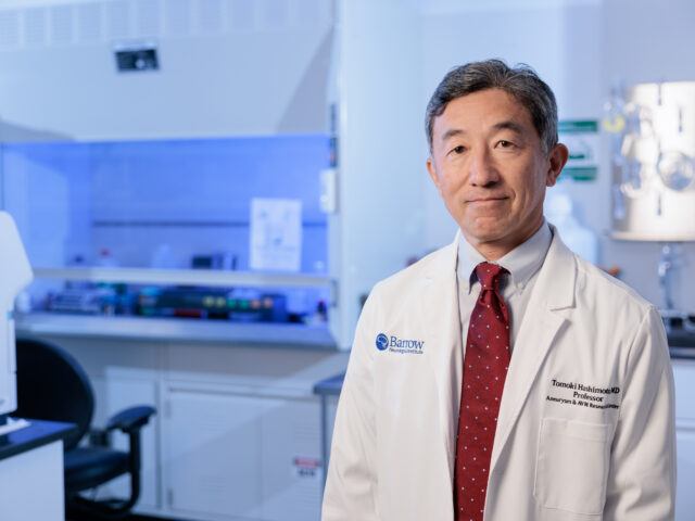 Dr. Tomoki Hashimoto poses in his laboratory in the Barrow Aneurysm and AVM Research Center. He is wearing a white lab coat.