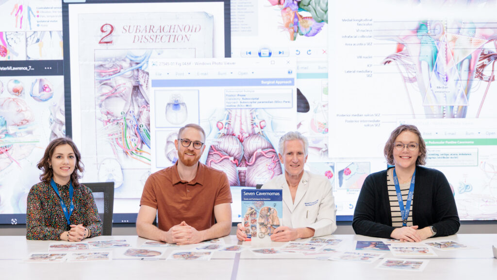 Dr. Lawton poses with his "Seven Cavernomas" textbook, alongside his medical illustration team in the Barrow Neuroscience Publications department. Illustrations from the book are displayed in the background and on the table in front of them.
