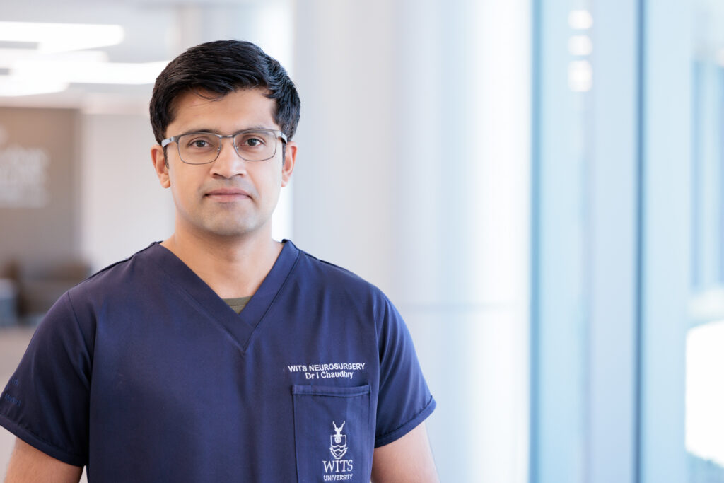 Irtiza Chaudhry, MD, in a brightly lit lobby at Barrow. He is wearing scrubs and smiling softly at the camera.