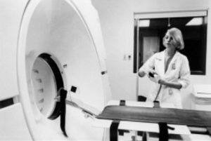 A black and white photo of a woman operating a CT scanner