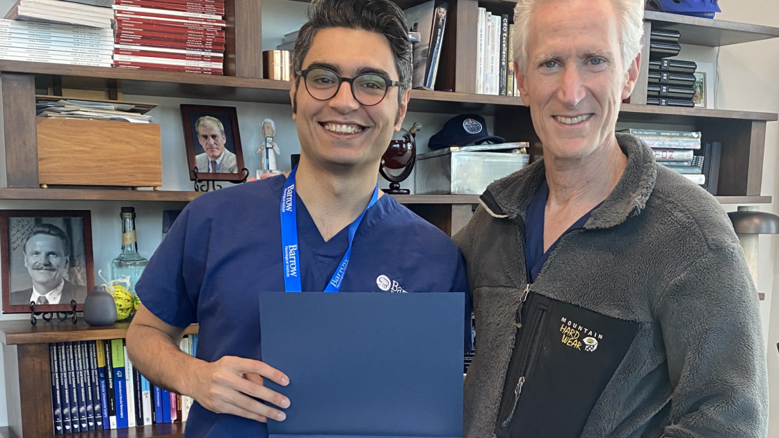 Dr. Mammadli poses for a photo with Dr. Lawton in Dr. Lawton's office. Dr. Mammadli is holding his certificate, recognizing his successful completion of his observership at Barrow.