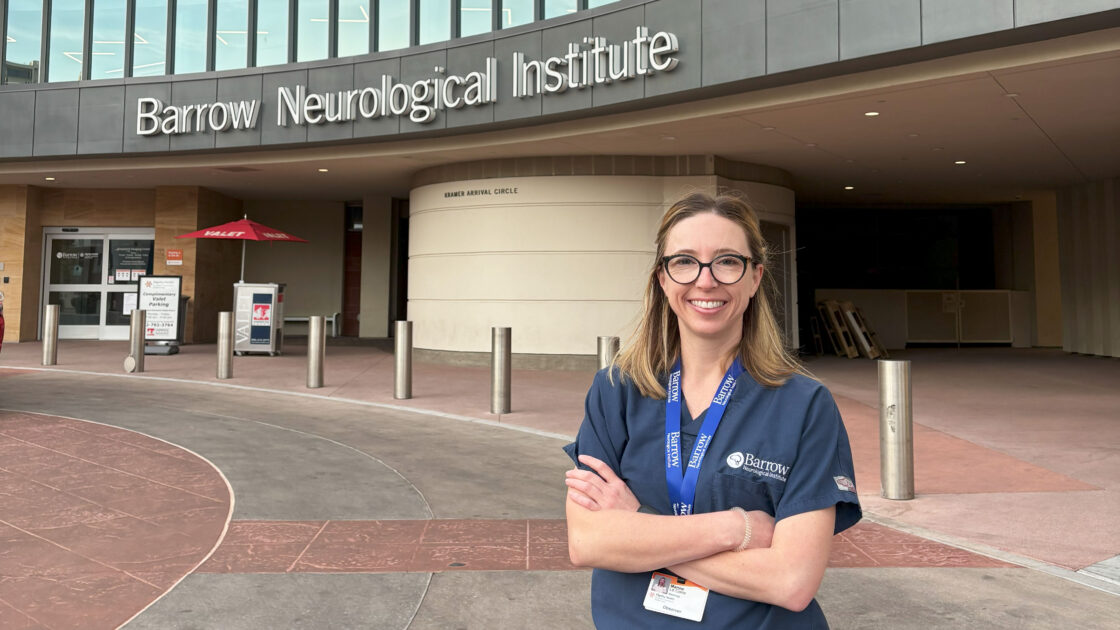 Dr. Marine Le Corre stands in front of the Barrow Neuroplex. She is smiling at the camera and has her arms folded.