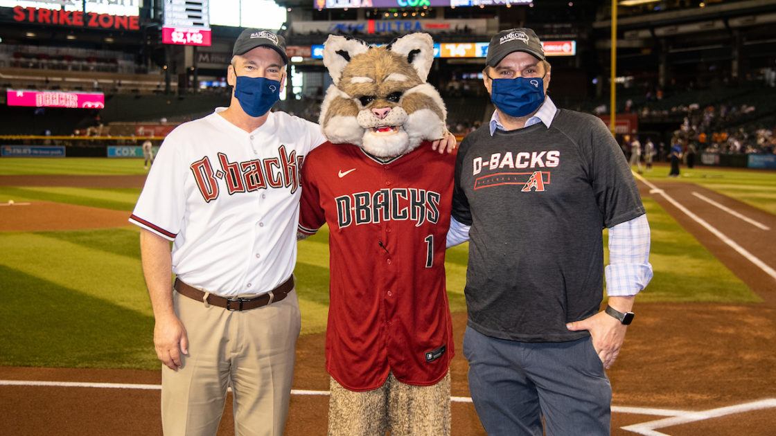 Dr. Robert Bowser and Dr. Fredric Manfredsson pose with Baxter the Bobcat, the Arizona Diamondbacks mascot, on the field