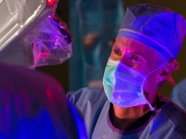 Dr. Michael T. Lawton is pictured in the OR, looking up from the microscope