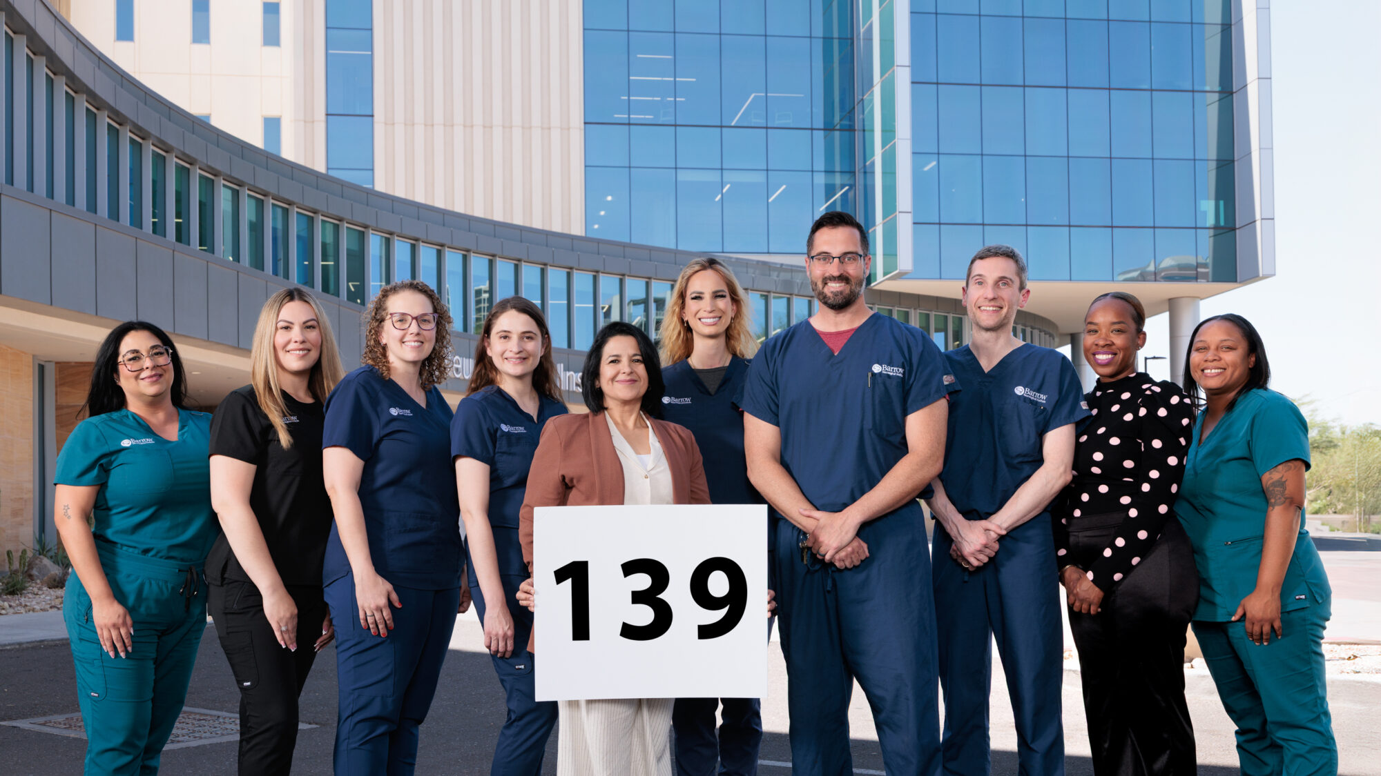Group photo in front of the Barrow Neuroplex showing the cochlear implant team holding a sign to commemorate the 139 implant surgeries completed in 2024.