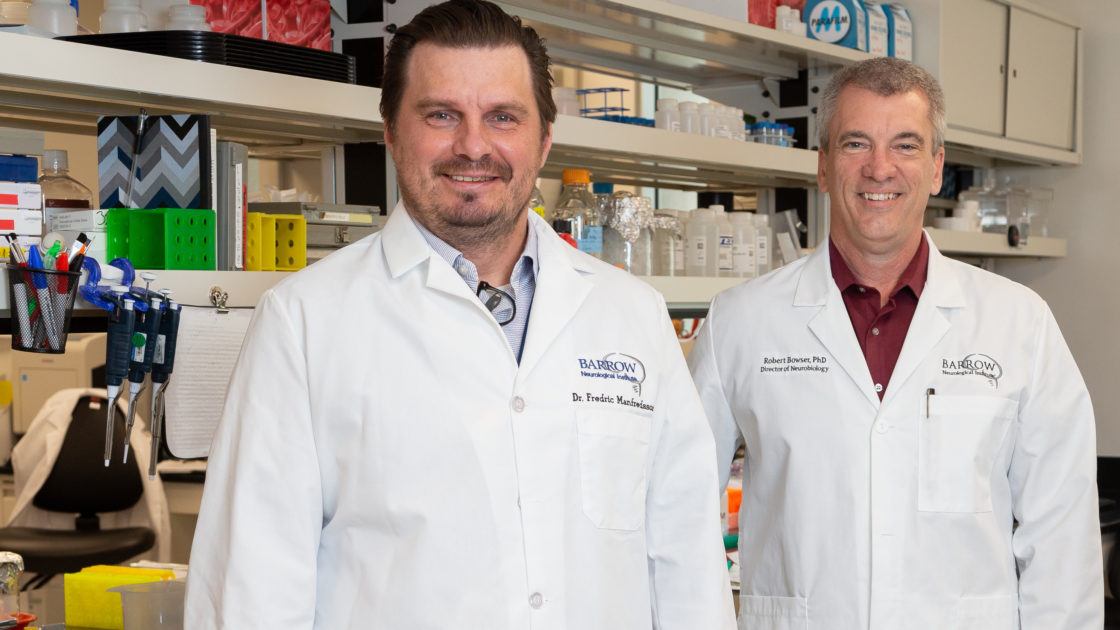 Dr. Fredric Manfredsson and Dr. Robert Bowser pose in a laboratory in their white coats.