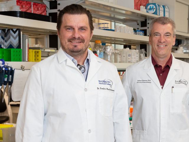 Dr. Fredric Manfredsson and Dr. Robert Bowser pose in a laboratory in their white coats.