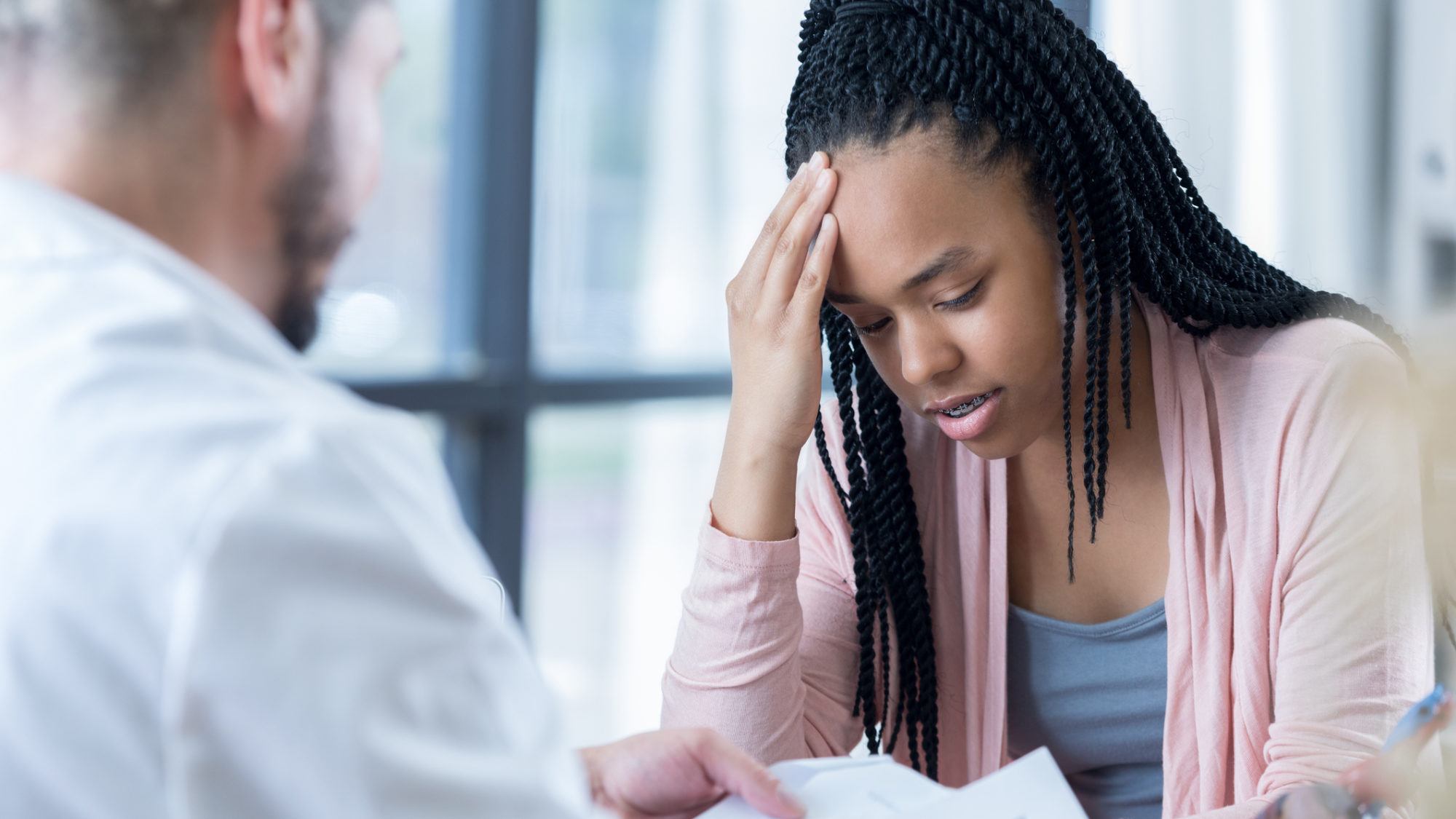 young patient talking to doctor with her hand on her head