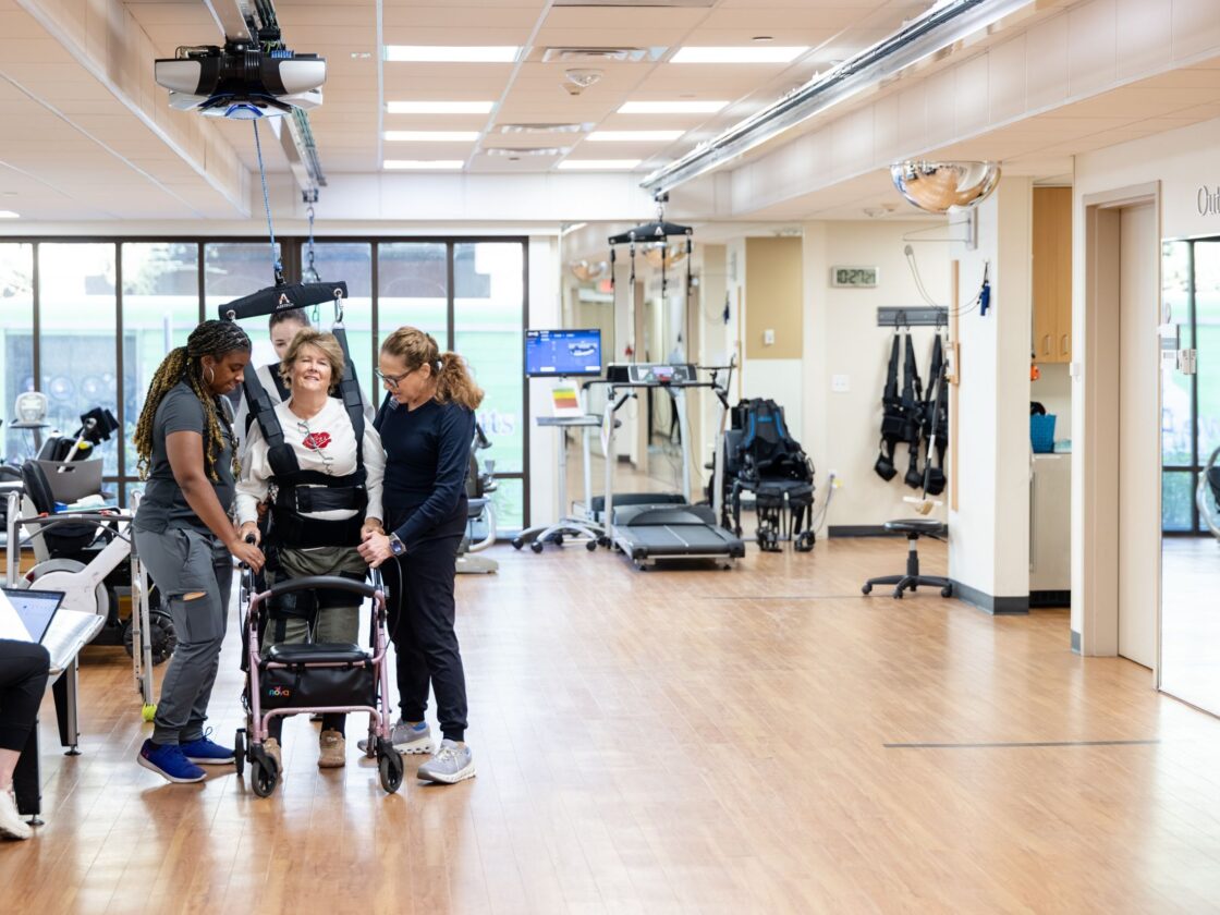 Barrow Neuro-Rehab patient walking with the help of their therapists and Zero Gravity balance system.
