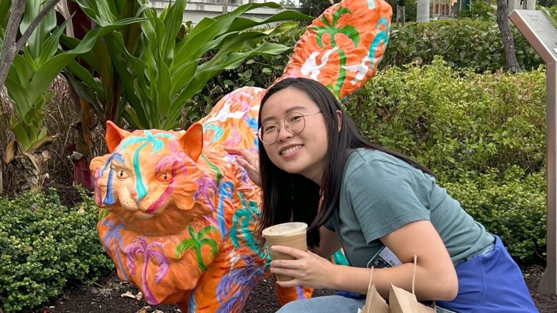 ruoyan zhu poses with coffee in front of a colorful cat statue