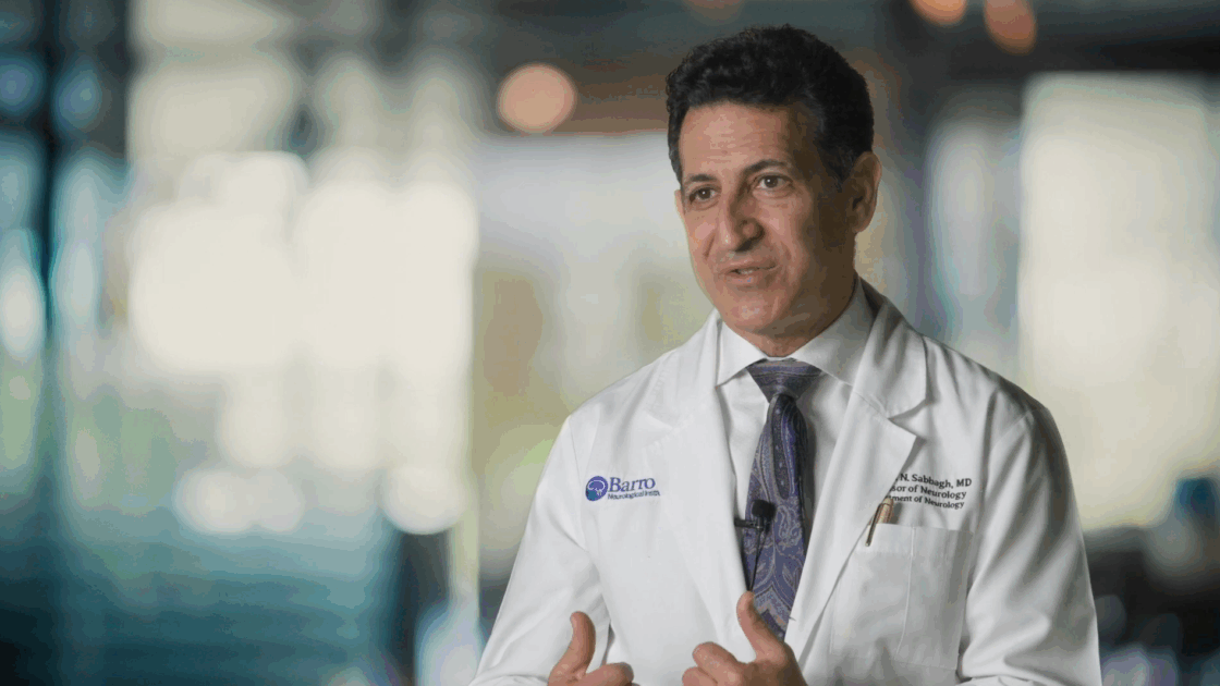 Still photo of Dr. Marwan Sabbagh during an interview. He is wearing a white, Barrow-branded lab coat. The backdrop is blurred.
