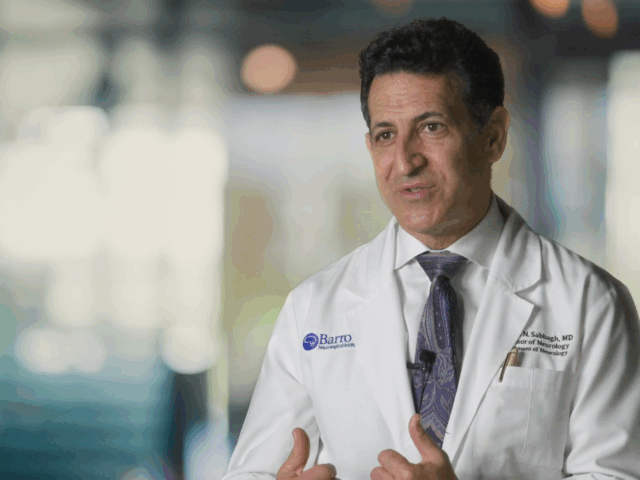 Still photo of Dr. Marwan Sabbagh during an interview. He is wearing a white, Barrow-branded lab coat. The backdrop is blurred.