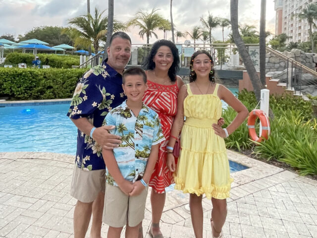 Sabrina Mancini and her family pose for a photo next to a swimming pool at a resort in Aruba.