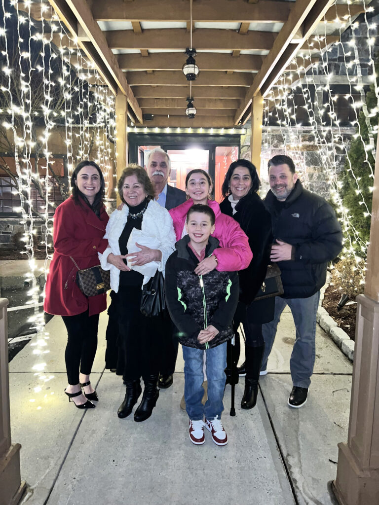 Photo of Sabrina with her family. They are huddled together underneath strings of Christmas lights.